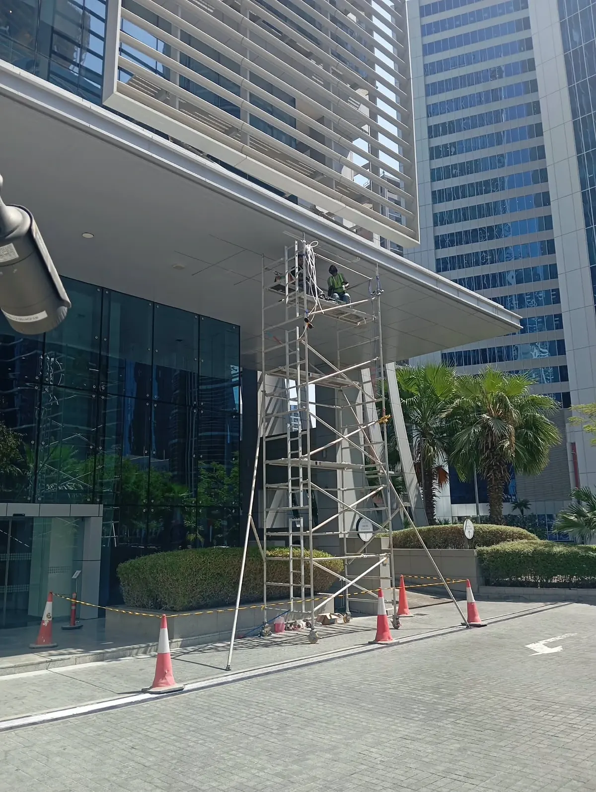 Mobile scaffold tower under a hotel entrance canopy, cordoned off with cones and tape