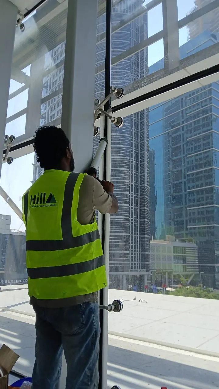 Hill technician rectifying a curtain-wall glazing fixing at Anantara Downtown, with Dubai towers behind