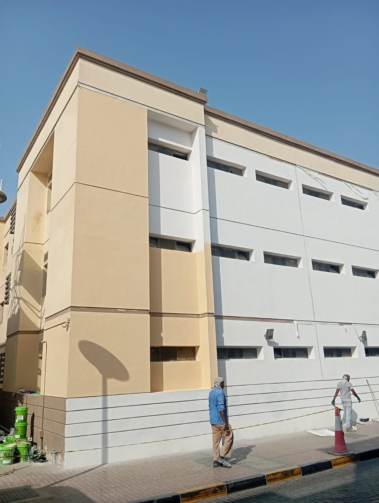 Building facade part-way through repainting, with painters and materials on site