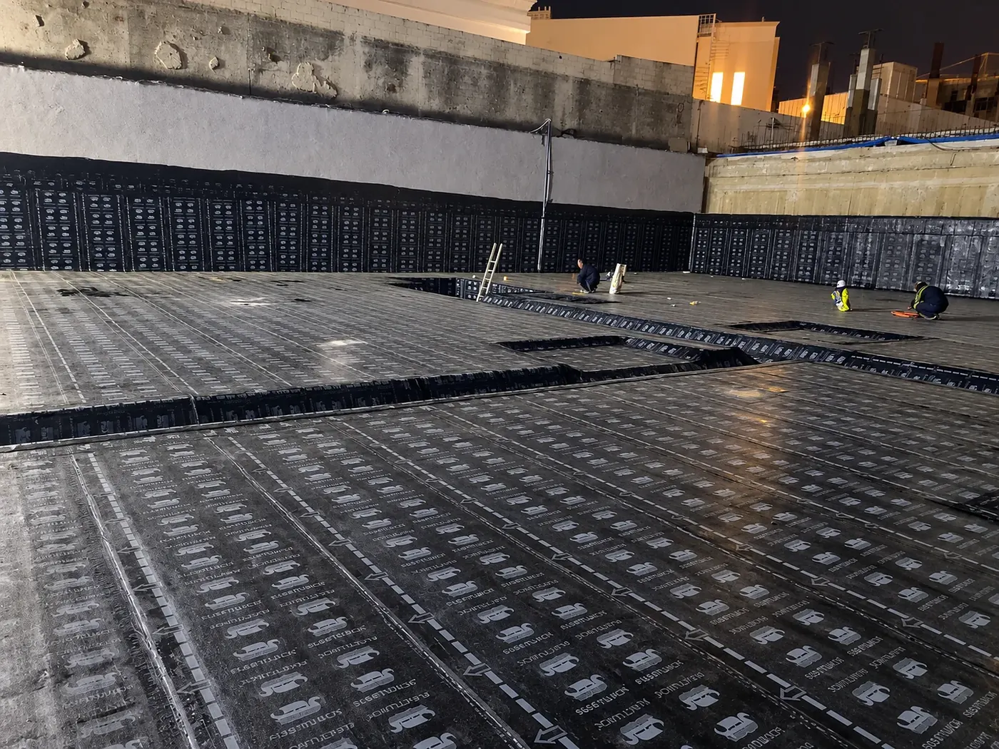 Torch-applied bituminous membrane being laid across a large slab and up the retaining walls
