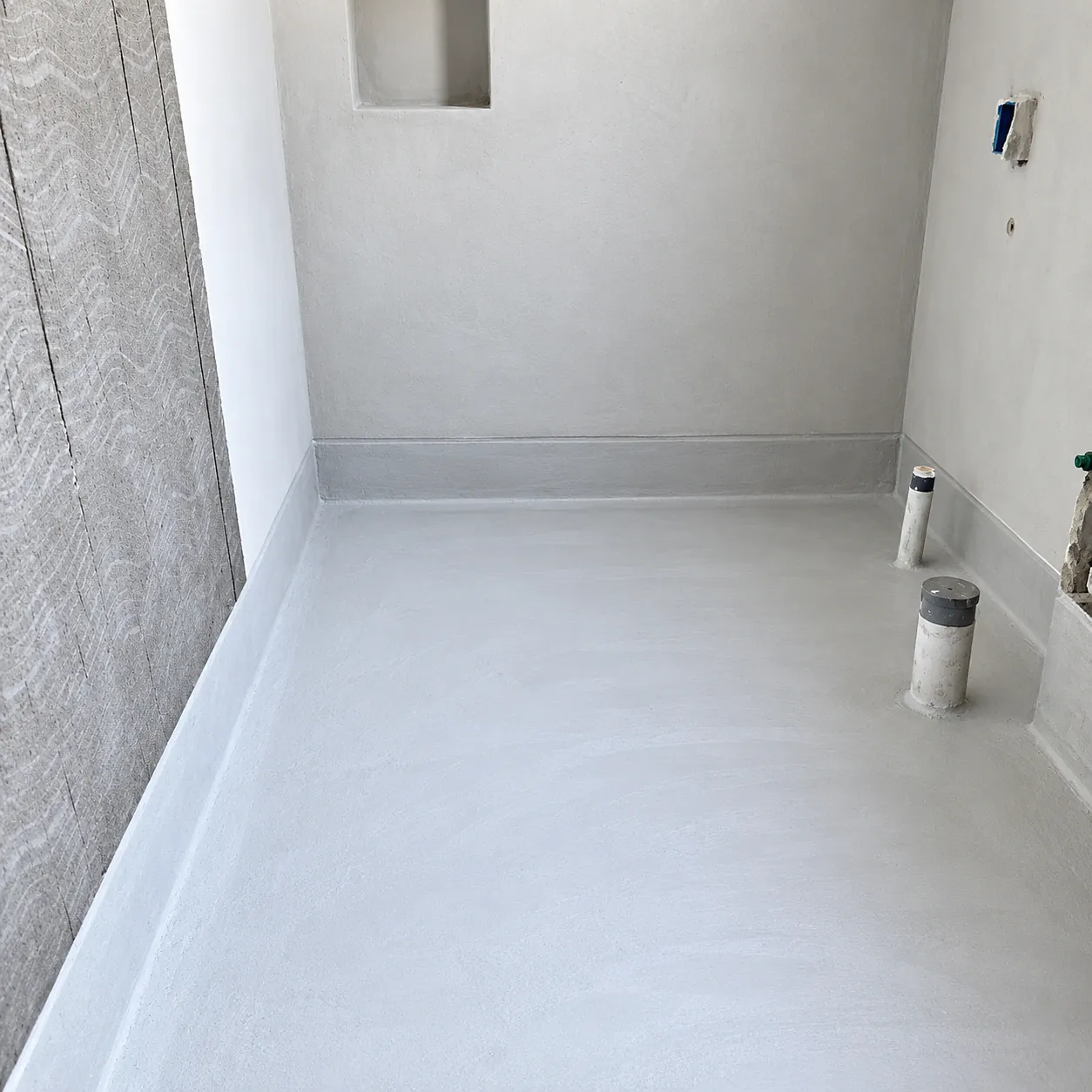 Wet room floor and wall upstands coated with cementitious waterproofing around pipe penetrations
